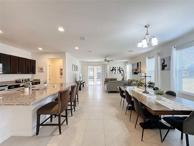 tiled dining area with ceiling fan with notable chandelier, sink, and a textured ceiling