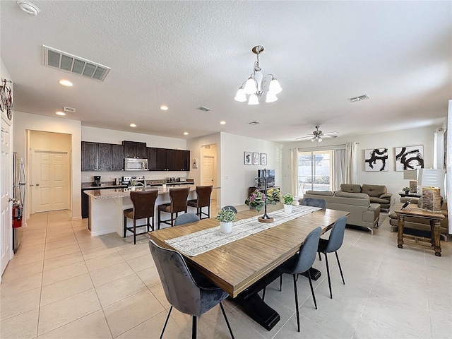 dining space with light tile patterned floors, ceiling fan with notable chandelier, and a textured ceiling