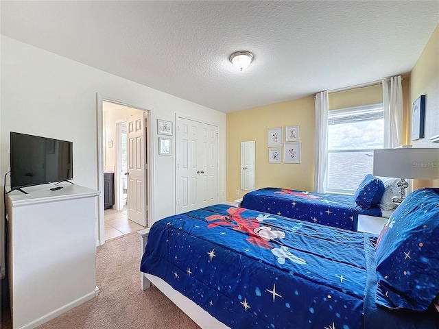 bedroom with light carpet, ensuite bath, and a textured ceiling