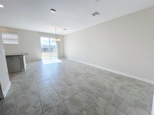 empty room featuring a chandelier, a textured ceiling, and light tile patterned flooring