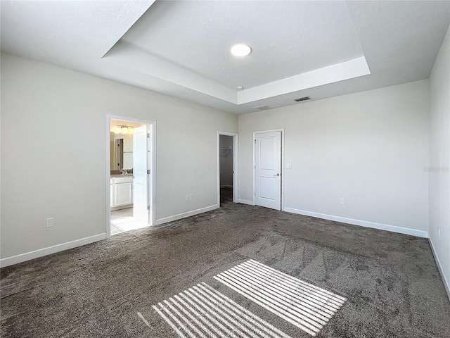 unfurnished bedroom featuring connected bathroom, carpet floors, a raised ceiling, and a closet