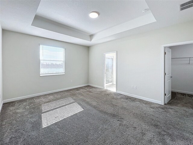 unfurnished bedroom featuring dark carpet, a walk in closet, a textured ceiling, a tray ceiling, and a closet