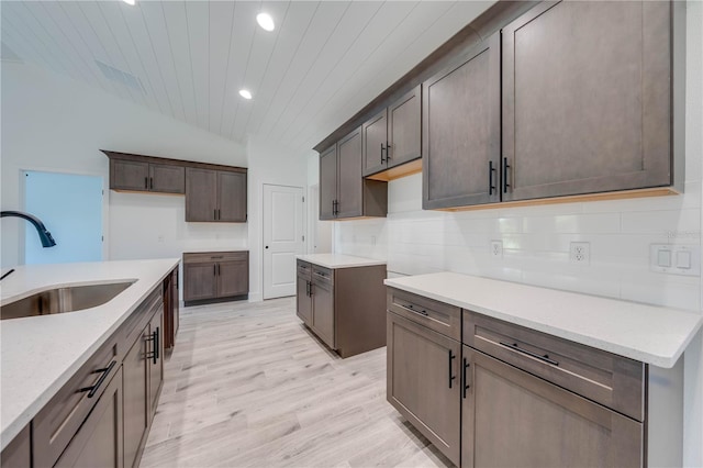 kitchen with light hardwood / wood-style floors, tasteful backsplash, light stone countertops, vaulted ceiling, and sink