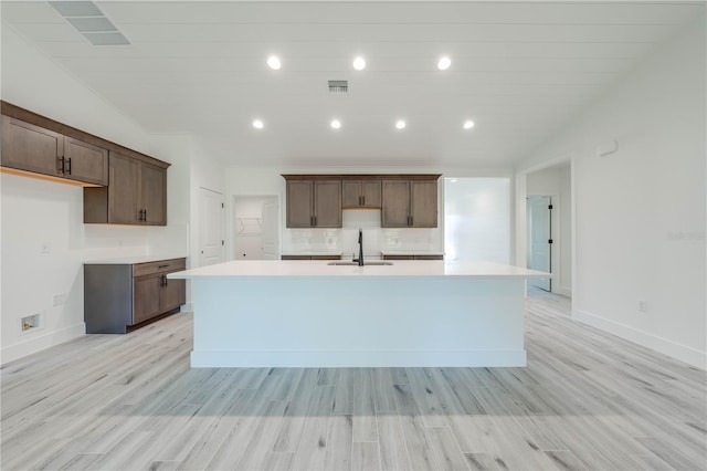 kitchen with light hardwood / wood-style floors, an island with sink, lofted ceiling, dark brown cabinets, and sink