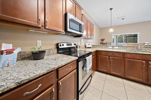 kitchen featuring sink, decorative light fixtures, light tile patterned floors, light stone countertops, and appliances with stainless steel finishes