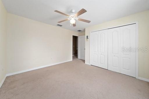 unfurnished bedroom featuring ceiling fan, a closet, and light carpet