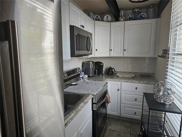 kitchen featuring appliances with stainless steel finishes, white cabinetry, backsplash, dark tile patterned floors, and beam ceiling