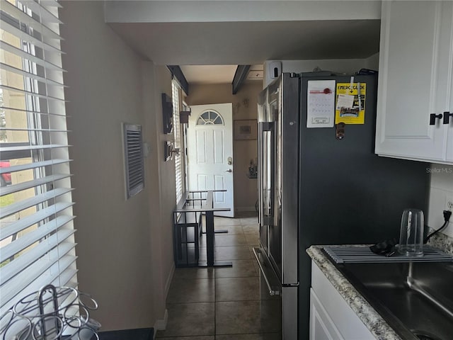 kitchen featuring light stone counters, dark tile patterned flooring, white cabinets, beamed ceiling, and sink