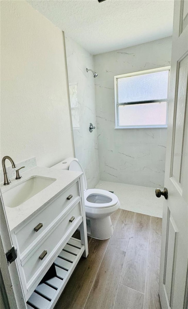 bathroom featuring a textured ceiling, toilet, a tile shower, and vanity