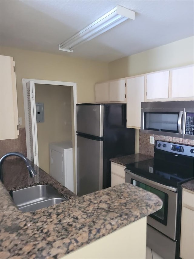 kitchen with stainless steel appliances, dark stone counters, decorative backsplash, sink, and white cabinetry