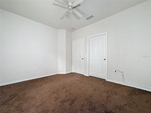 unfurnished bedroom featuring ceiling fan, dark carpet, and two closets