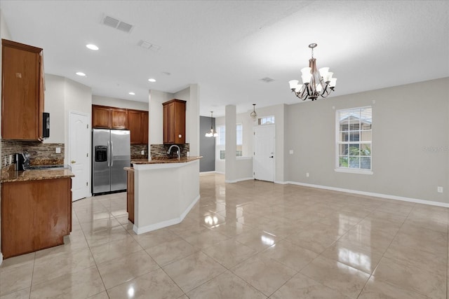 kitchen with a sink, appliances with stainless steel finishes, dark stone counters, tasteful backsplash, and an inviting chandelier