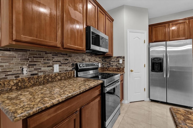 kitchen with stainless steel appliances, brown cabinetry, dark stone countertops, and decorative backsplash