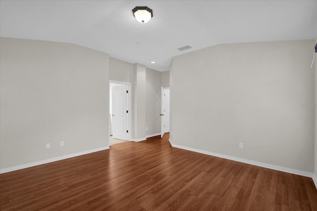 empty room with vaulted ceiling, wood finished floors, visible vents, and baseboards