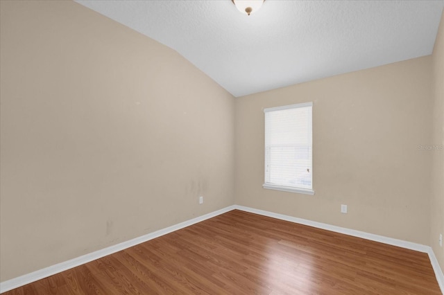 unfurnished room with vaulted ceiling, a textured ceiling, wood finished floors, and baseboards