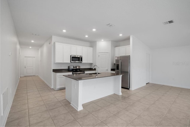 kitchen with appliances with stainless steel finishes, white cabinetry, sink, light tile patterned floors, and a center island with sink