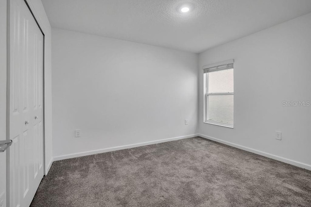 unfurnished bedroom with a closet, dark carpet, and a textured ceiling