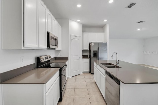 kitchen with light tile patterned floors, stainless steel appliances, a kitchen island with sink, white cabinets, and sink