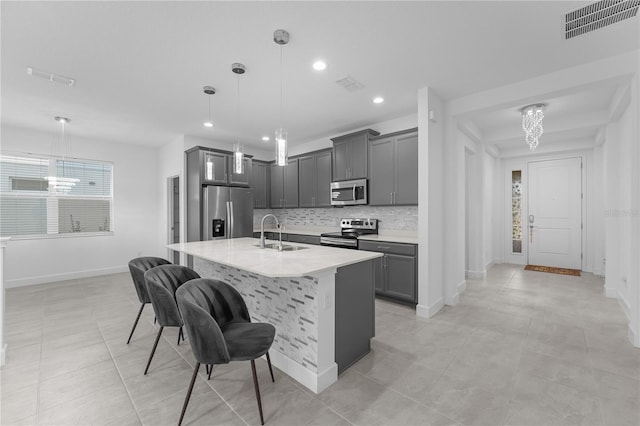 kitchen with decorative light fixtures, stainless steel appliances, an island with sink, gray cabinetry, and sink