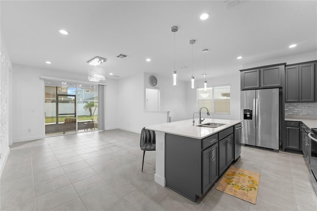 kitchen with decorative light fixtures, stainless steel appliances, a center island with sink, and sink