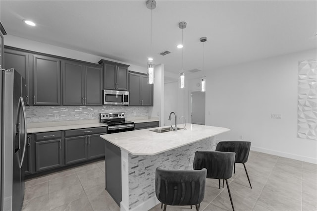 kitchen with a kitchen breakfast bar, appliances with stainless steel finishes, hanging light fixtures, an island with sink, and decorative backsplash