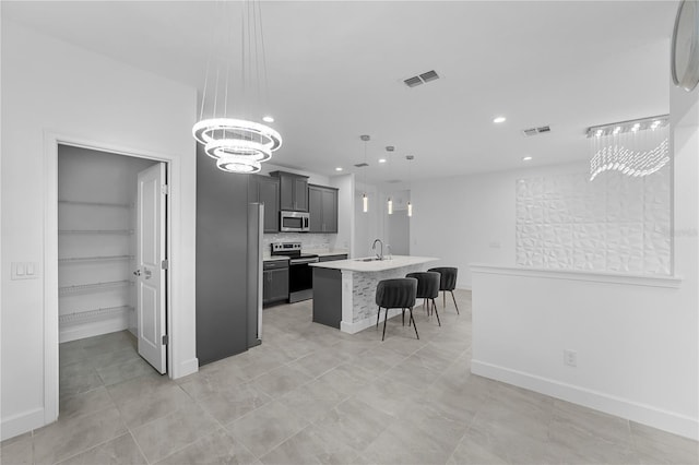 kitchen with a kitchen island with sink, a chandelier, stainless steel appliances, sink, and decorative light fixtures