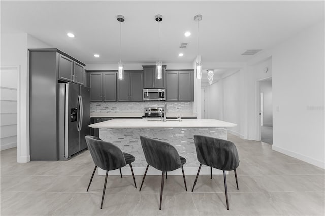 kitchen with pendant lighting, a center island with sink, tasteful backsplash, gray cabinetry, and appliances with stainless steel finishes