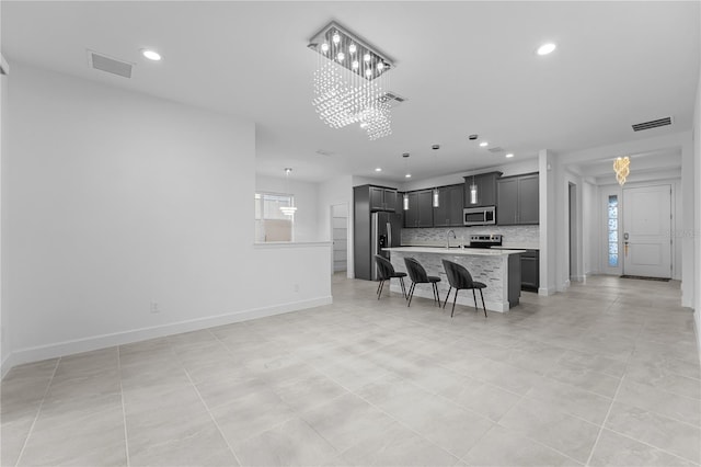 kitchen with stainless steel appliances, a kitchen bar, a kitchen island with sink, backsplash, and sink