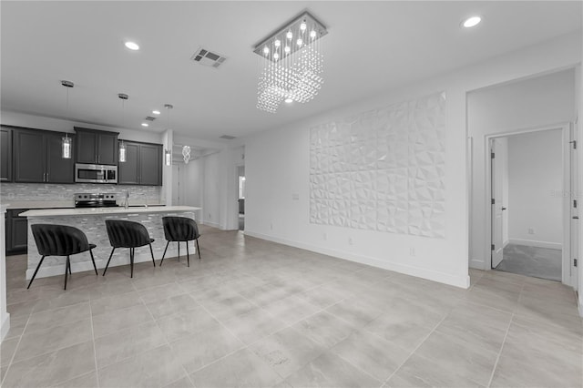 kitchen with a breakfast bar, pendant lighting, backsplash, a kitchen island with sink, and appliances with stainless steel finishes