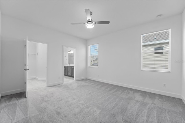 unfurnished bedroom with a spacious closet, a closet, connected bathroom, ceiling fan, and light carpet