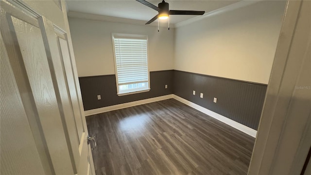 unfurnished bedroom featuring a wainscoted wall, crown molding, dark wood-type flooring, a ceiling fan, and baseboards