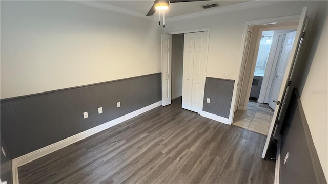 unfurnished bedroom featuring visible vents, dark wood finished floors, a wainscoted wall, ceiling fan, and a closet