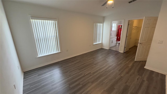 unfurnished bedroom featuring a closet, dark wood-style flooring, a walk in closet, and baseboards