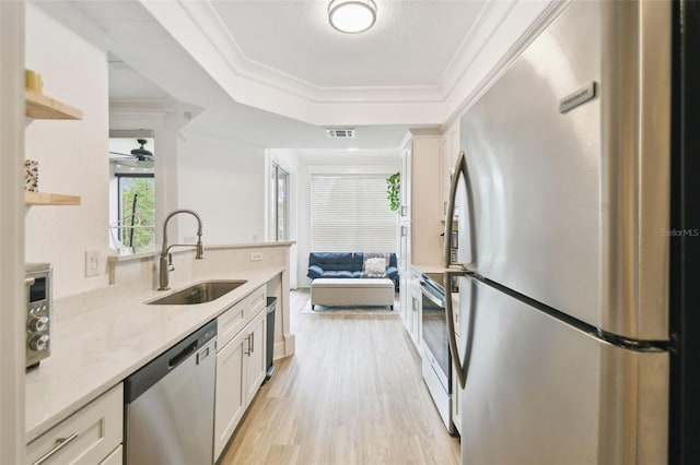 kitchen with appliances with stainless steel finishes, light wood-type flooring, white cabinets, light stone counters, and sink