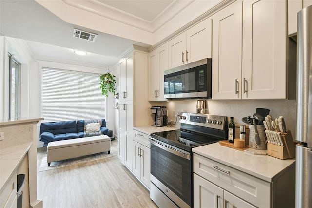 kitchen with light wood-type flooring, appliances with stainless steel finishes, ornamental molding, and light stone counters