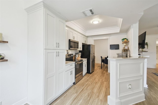 kitchen featuring white cabinetry, light hardwood / wood-style floors, stainless steel appliances, a raised ceiling, and ornamental molding