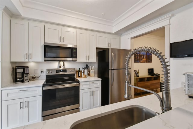 kitchen with light stone countertops, white cabinetry, appliances with stainless steel finishes, and crown molding