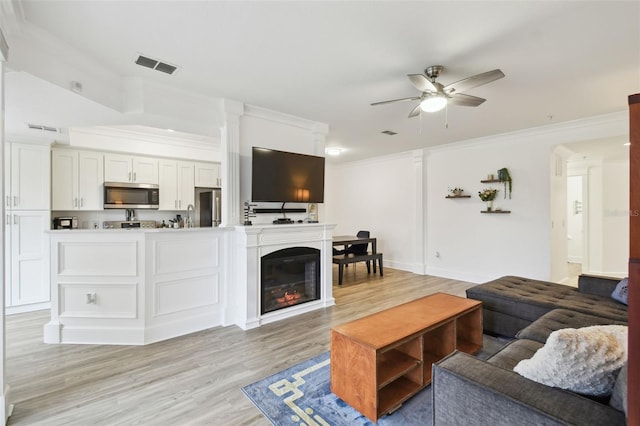 living room with light wood-type flooring, ceiling fan, and ornamental molding