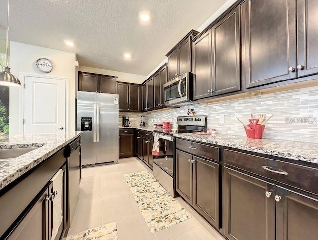 kitchen with stainless steel appliances, light tile patterned floors, tasteful backsplash, dark brown cabinets, and hanging light fixtures