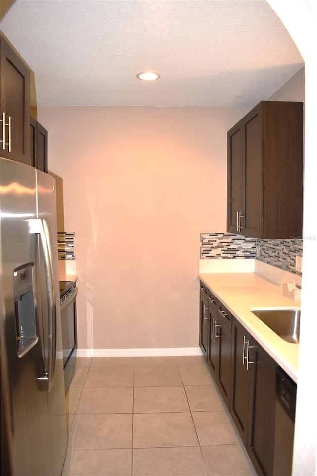 kitchen with sink, appliances with stainless steel finishes, backsplash, dark brown cabinetry, and light tile patterned flooring