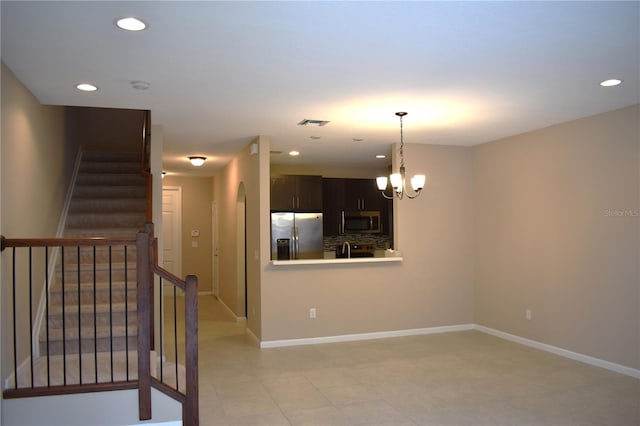 interior space featuring decorative backsplash, kitchen peninsula, stainless steel appliances, dark brown cabinets, and an inviting chandelier