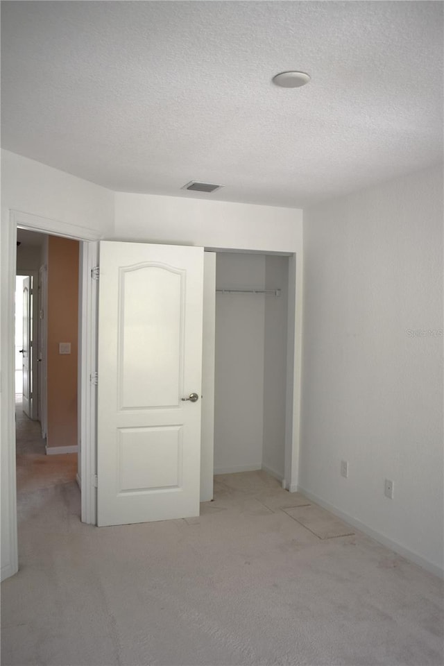 unfurnished bedroom with light colored carpet, a textured ceiling, and a closet