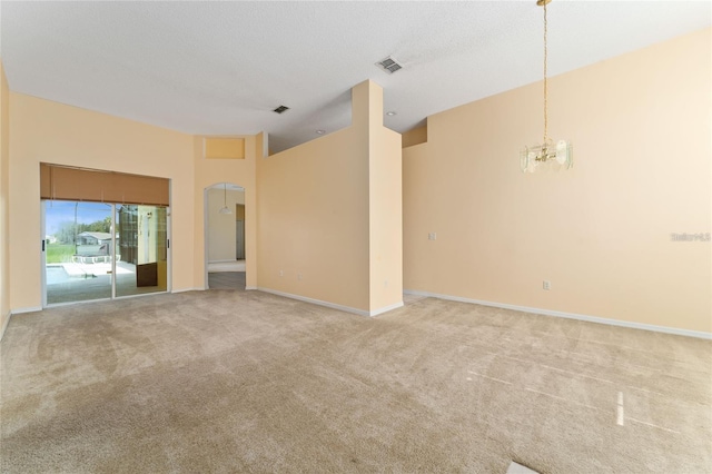 empty room featuring a towering ceiling, light carpet, and a chandelier