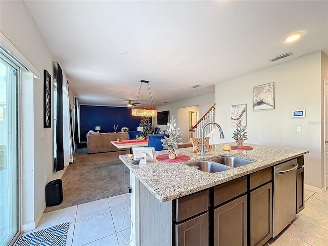 kitchen featuring sink, stainless steel dishwasher, dark brown cabinetry, light stone counters, and a center island with sink