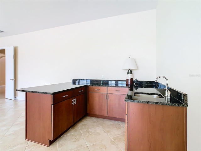 kitchen featuring kitchen peninsula, dark stone counters, and sink