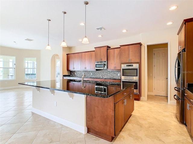 kitchen featuring decorative light fixtures, stainless steel appliances, tasteful backsplash, an island with sink, and light tile patterned flooring