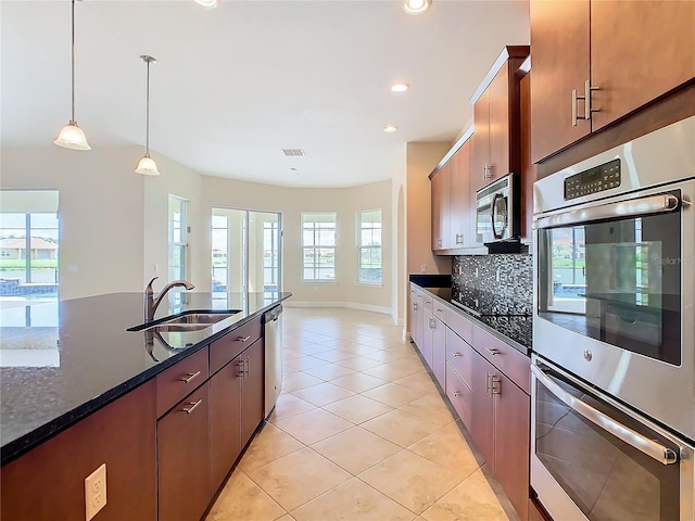 kitchen featuring appliances with stainless steel finishes, decorative light fixtures, dark stone counters, tasteful backsplash, and sink