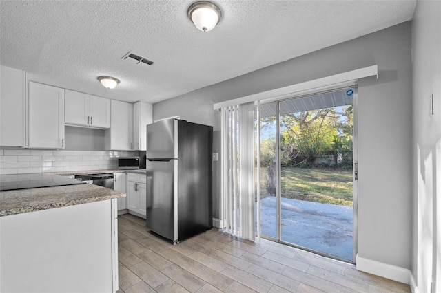 kitchen featuring backsplash, white cabinets, light wood-type flooring, a textured ceiling, and stainless steel appliances