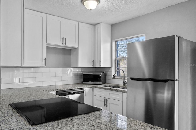 kitchen featuring light stone countertops, appliances with stainless steel finishes, backsplash, sink, and white cabinets