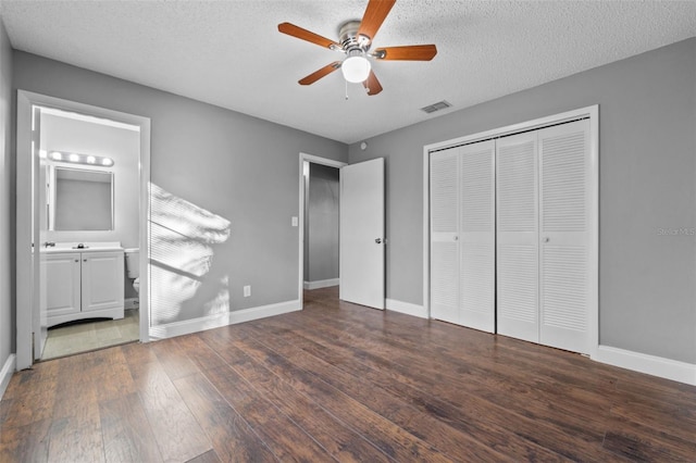 unfurnished bedroom featuring dark hardwood / wood-style flooring, ensuite bathroom, a textured ceiling, ceiling fan, and a closet